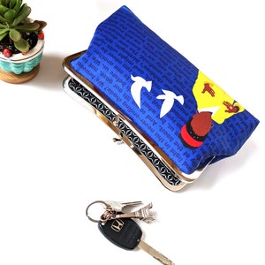 The Amanda Gorman clutch purse is shown from above, slightly opened. There is a set of keys on front and a plant off to the side. The inside of the clutch is black with a white design.