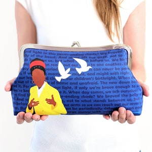 The model is holding the Amanda Gorman clutch purse in front of her.