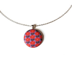The fabric pendant necklace is hanging from a silver colored chain. The pendant has a light purple background with a pattern of red flowers.
