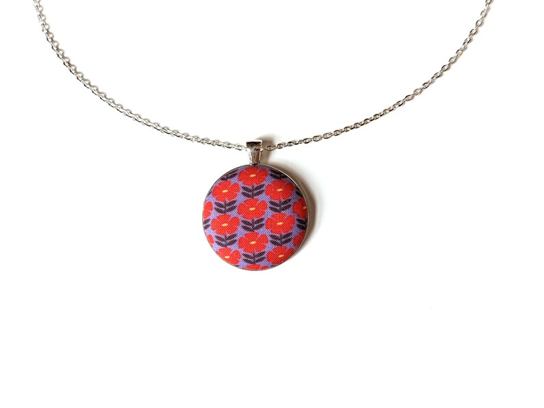 The fabric pendant necklace is hanging from a silver colored chain. The pendant has a light purple background with a pattern of red flowers.