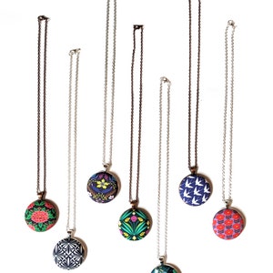 Seven different colorful fabric pendant necklaces are shown from above on a white background.