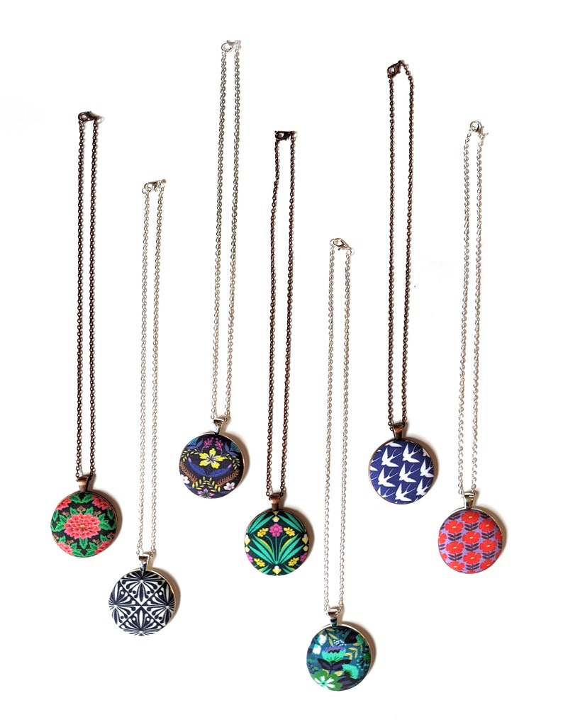 Seven different colorful fabric pendant necklaces are shown from above on a white background.