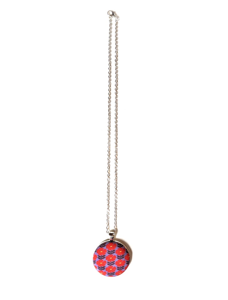 The fabric pendant necklace is hanging from a silver colored chain. The pendant has a light purple background with a pattern of red flowers.