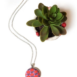 The floral fabric necklace is shown from above on a white background, next to a green plant.