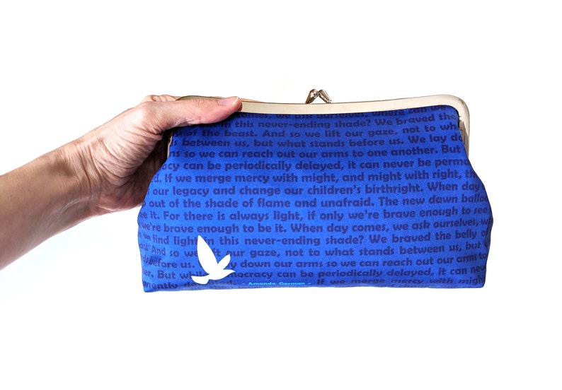 The model's hand is holding out the clutch. The back of the clutch is shown. It is blue with dark blue text. There is a single white bird near the bottom.