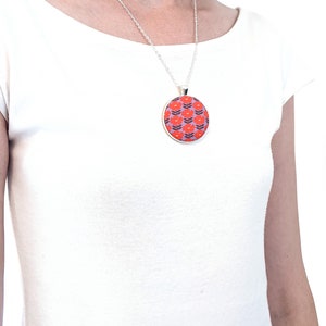 The model is wearing the fabric pendant necklace. The pendant falls to about mid-chest.