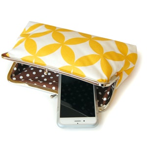 The yellow and white clutch is shown on its side, slightly opened. Inside there is a brown and white polka dot print. There is a phone resting inside the bag.