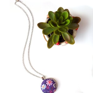 The necklace is shown from above next to a green plant.