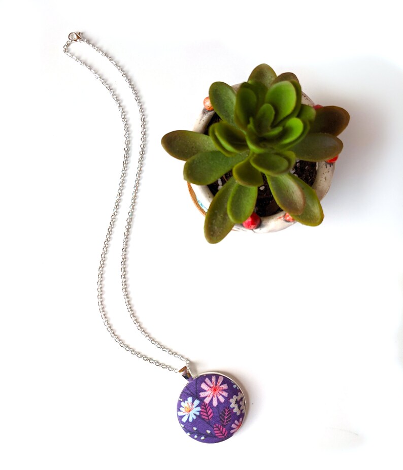 The necklace is shown from above next to a green plant.