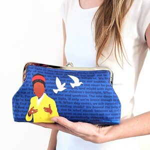 The model is holding the Amanda Gorman clutch purse in front of her.