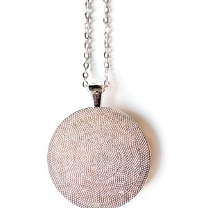 A close up view of the back of the silver colored circle shaped pendant.