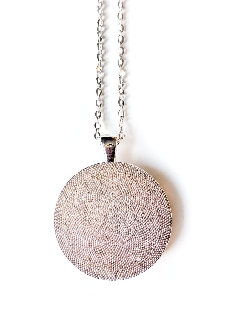 A close up view of the back of the silver colored circle shaped pendant.