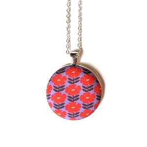 The fabric pendant necklace is hanging from a silver colored chain. The pendant has a light purple background with a pattern of red flowers.