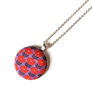 The fabric pendant necklace is hanging from a silver colored chain. The pendant has a light purple background with a pattern of red flowers.