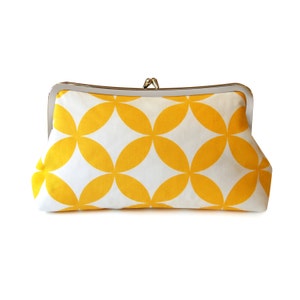 The yellow and white geometric clutch sits on a white background. The clutch has a silver colored clasp at the top.