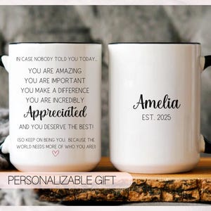 May include: Two white ceramic mugs with black handles and rims. One mug has the text "In case nobody told you today... You are amazing... Appreciated..." The other mug has the name "Amelia" and "EST. 2025".