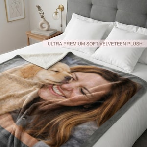 May include: A plush blanket with a printed image of a woman smiling and a golden retriever puppy. The blanket has a soft, velvety texture and a gray border. The text "ULTRA PREMIUM SOFT VELVETEEN PLUSH" is printed on the blanket.
