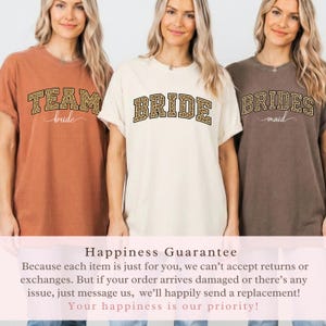 May include: Three women wearing matching t-shirts. The shirts are in shades of orange, cream, and brown. The text on the shirts reads "TEAM bride", "BRIDE", and "BRIDES maid" in a bold, leopard print font. The shirts are for a bridal party.