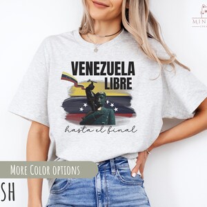 May include: A gray t-shirt with a graphic design featuring a Venezuelan flag, a soldier, and the text "Venezuela Libre hasta el final".