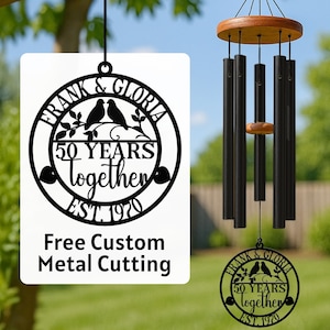 May include: A black metal wind chime with a wooden top and striker. The chime has black tubes and a decorative metal piece with the text "FRANK & GLORIA 50 YEARS together EST. 1970". A white sign reads "Free Custom Metal Cutting".