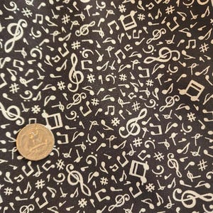 May include: Black fabric with a repeating pattern of white musical notes, including treble clefs, eighth notes, and sharps. A quarter coin is visible in the lower left corner, providing a size reference. The fabric has a musical theme.