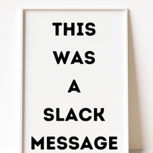 May include: A framed white print with the text "THIS WAS A SLACK MESSAGE" in bold, black letters. The artwork is displayed against a white wall.