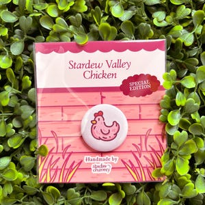 May include: A round, white pin featuring a pink chicken illustration, set against a pink brick wall design. The pin is labeled "Stardew Valley Chicken" with a "Special Edition" tag. The card also includes "Handmade by studio charmy".