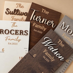 May include: A collection of rectangular wooden growth charts featuring raised 3D lettering for family names such as The Sullivan Family, The Turner Family, The Rogers Family, and The Watson Family, with engraved measurement markings and established dates.
