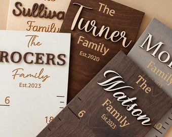 May include: A collection of rectangular wooden growth charts featuring raised 3D lettering for family names such as The Sullivan Family, The Turner Family, The Rogers Family, and The Watson Family, with engraved measurement markings and established dates.