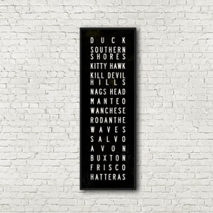Peut inclure: Impression typographique en noir et blanc sur fond noir listant les noms de diff&eacute;rentes villes et villages le long des Outer Banks de Caroline du Nord. Le texte indique : Duck, Southern Shores, Kitty Hawk, Kill Devil Hills, Nags Head, Manteo, Wanchese, Rodanthe, Waves, Salvo, Avon, Buxton, Frisco, Hatteras.