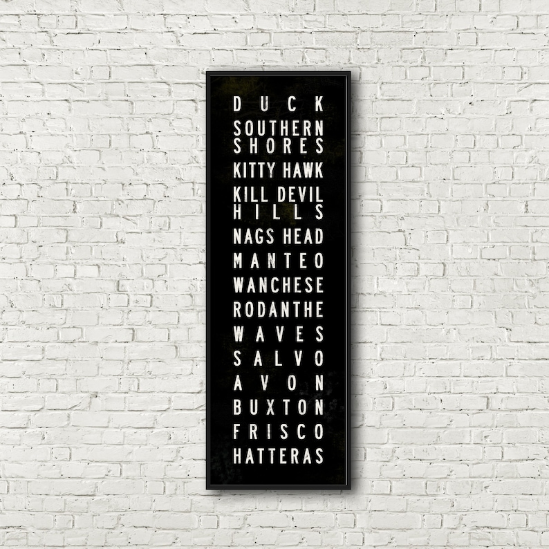 Peut inclure: Impression typographique en noir et blanc sur fond noir listant les noms de diff&eacute;rentes villes et villages le long des Outer Banks de Caroline du Nord. Le texte indique : Duck, Southern Shores, Kitty Hawk, Kill Devil Hills, Nags Head, Manteo, Wanchese, Rodanthe, Waves, Salvo, Avon, Buxton, Frisco, Hatteras.