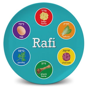 May include: A round, turquoise plate featuring the name "Rafi" in white, surrounded by circular illustrations of traditional Passover Seder plate items. Includes "bitter herbs," an egg, lettuce, charoset, a shank bone, and parsley.