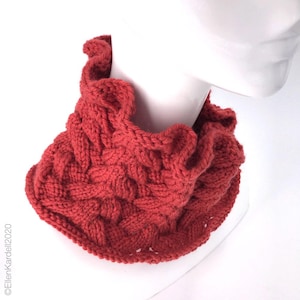 May include: A red knitted neck warmer with a cable knit pattern and a ruffled edge.