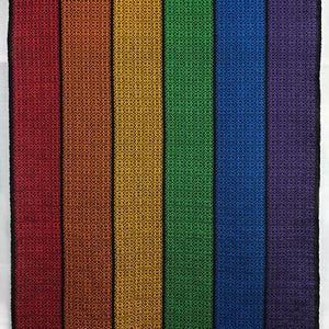 May include: A woven textile with a rainbow color scheme, featuring vertical stripes of red, orange, yellow, green, blue, and purple. The edges are black, and the bottom has matching colored fringe. The pattern is a repeating geometric design.