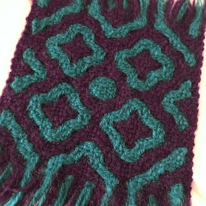Puede incluir: Primer plano de una tela de punto con un patrón geométrico. La tela es de color morado oscuro con formas geométricas de color turquesa.