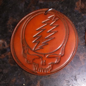 May include: A brown leather keychain with a Grateful Dead Steal Your Face logo. The logo is embossed in the leather and features a lightning bolt design.
