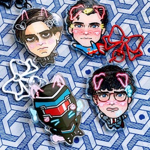 Op de afbeelding: Een verzameling acryl sleutelhangers met cartoonportretten met roze accenten. De sleutelhangers tonen verschillende personages met kattenoordesigns, blush en andere decoratieve elementen. Een rode strik sleutelhanger is ook inbegrepen.