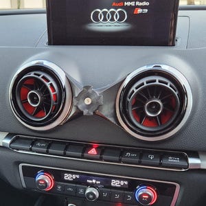 Puede incluir: Salpicadero de coche con rejillas de ventilación, controles de climatización y una pantalla. Las rejillas tienen un borde plateado y detalles en rojo. La pantalla muestra el logotipo de Audi y "Audi MMI Radio S3". El control de clima muestra una temperatura de 22,0 grados Celsius.