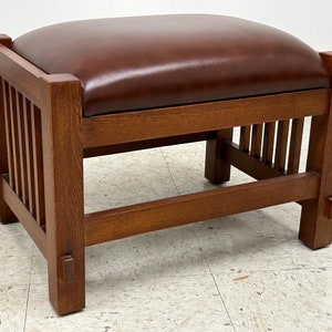 May include: A brown leather-topped footstool with a wooden frame. The frame has a slatted design and the legs are square.