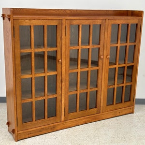 May include: A wooden bookcase with three glass doors and multiple shelves. The bookcase is a light brown color and has a simple design.