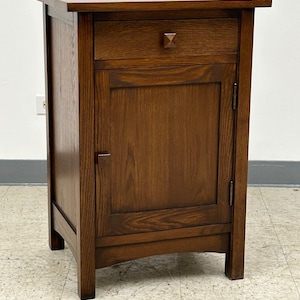May include: A dark brown wooden cabinet with a single drawer and a door. The cabinet has a simple, traditional design with a slightly curved base.