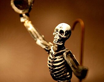May include: A skeletal figure wearing a top hat and holding a cane. The figure is made of white plastic and has a brown painted finish. The figure is posed with its arm raised and the hat tilted back.