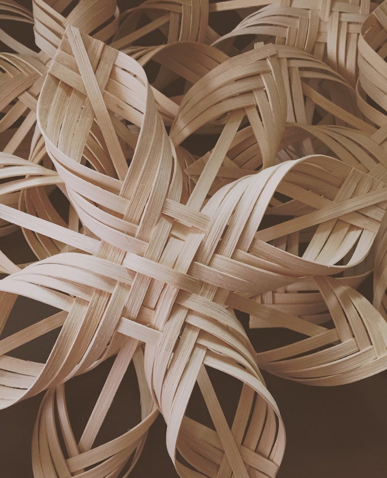 May include: A close-up of a woven star made from natural wood. The star is made of thin strips of wood that are woven together to create a complex pattern. The star is a light brown colour and has a natural, rustic look.
