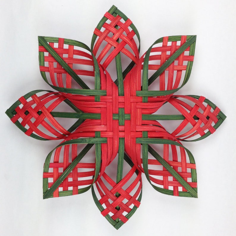 Puede incluir: Un adorno de estrella tejido de color rojo y verde. La estrella est&aacute; hecha de finas tiras de material tejido, creando un patr&oacute;n geom&eacute;trico.