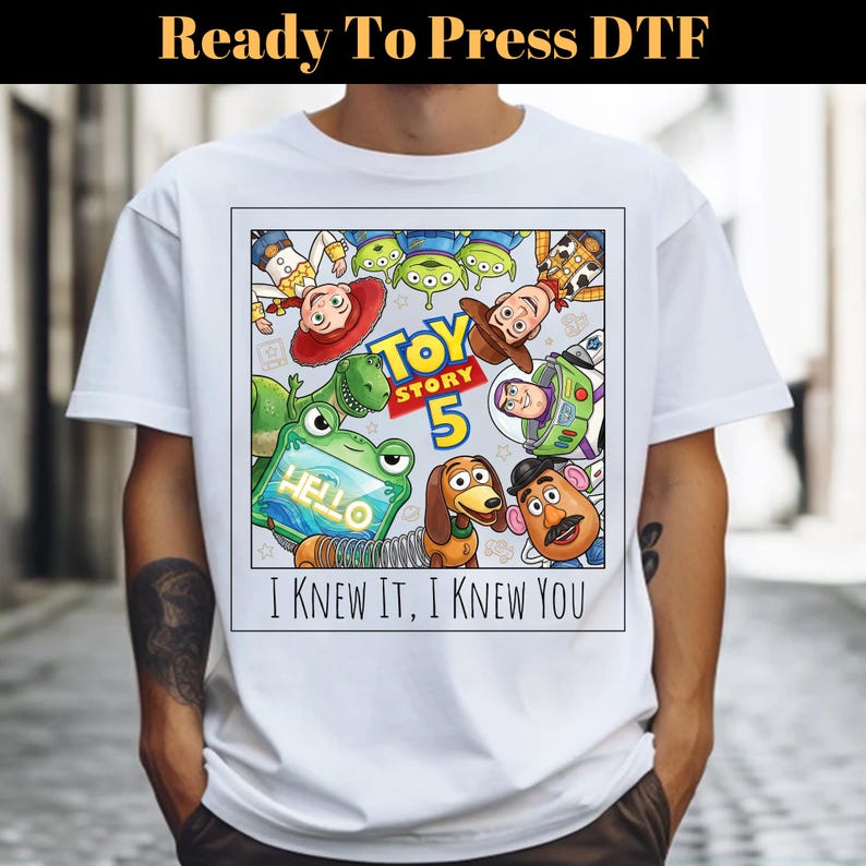 May include: A white t-shirt featuring a rectangular graphic print of Toy Story 5 characters including Woody, Buzz Lightyear, Jessie, Rex, Slinky Dog, Mr. Potato Head, and aliens. The text reads Toy Story 5 and I KNEW IT, I KNEW YOU.