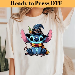 May include: A white t-shirt with a blue Stitch character wearing a witch hat and holding a book. The character is wearing a red and yellow scarf. The text "Ready to Press DTF" is at the top of the image.