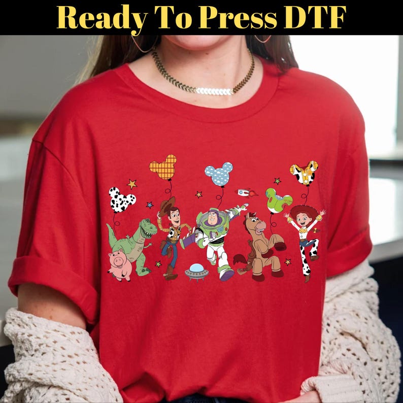 Puede incluir: Camiseta roja con un gr&aacute;fico colorido de personajes de una pel&iacute;cula animada popular. El dise&ntilde;o incluye personajes de dibujos animados, globos y el texto "Ready To Press DTF". Es una prenda de vestir casual.