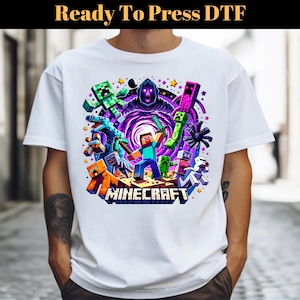 Może przedstawiać: Biała koszulka z kolorową grafiką postaci z Minecrafta, w tym Creepera, zombie, szkieleta i postaci gracza. Grafika jest otoczona gwiazdami i wirującym fioletowym wirkiem. Tekst "MINECRAFT" jest nadrukowany pod grafiką.