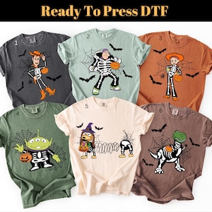 May include: Six t-shirts in various colours featuring Halloween-themed graphics of cartoon characters dressed in skeleton costumes with spiderwebs, bats, and pumpkins. The shirts are numbered one through six and include the text Ready To Press DTF.