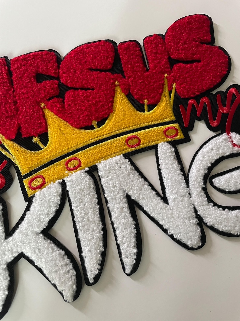 May include: Embroidered patch with the words "JESUS MY KING" in red and white, with a gold crown. The letters have a textured, fuzzy appearance, and the patch has a black border.